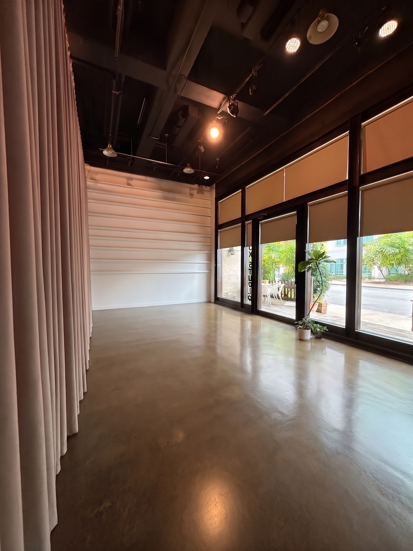 The full room at A39-1: a dark open ceiling with track lights, a long pleated curtain, and floor-to-ceiling street-facing windows